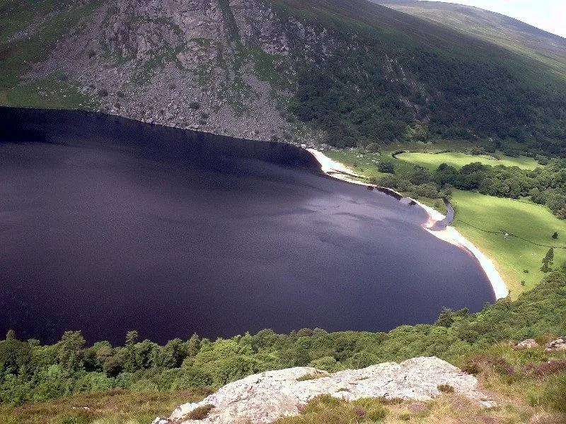 Dark water and a pale shore at Lough Tay seen from above